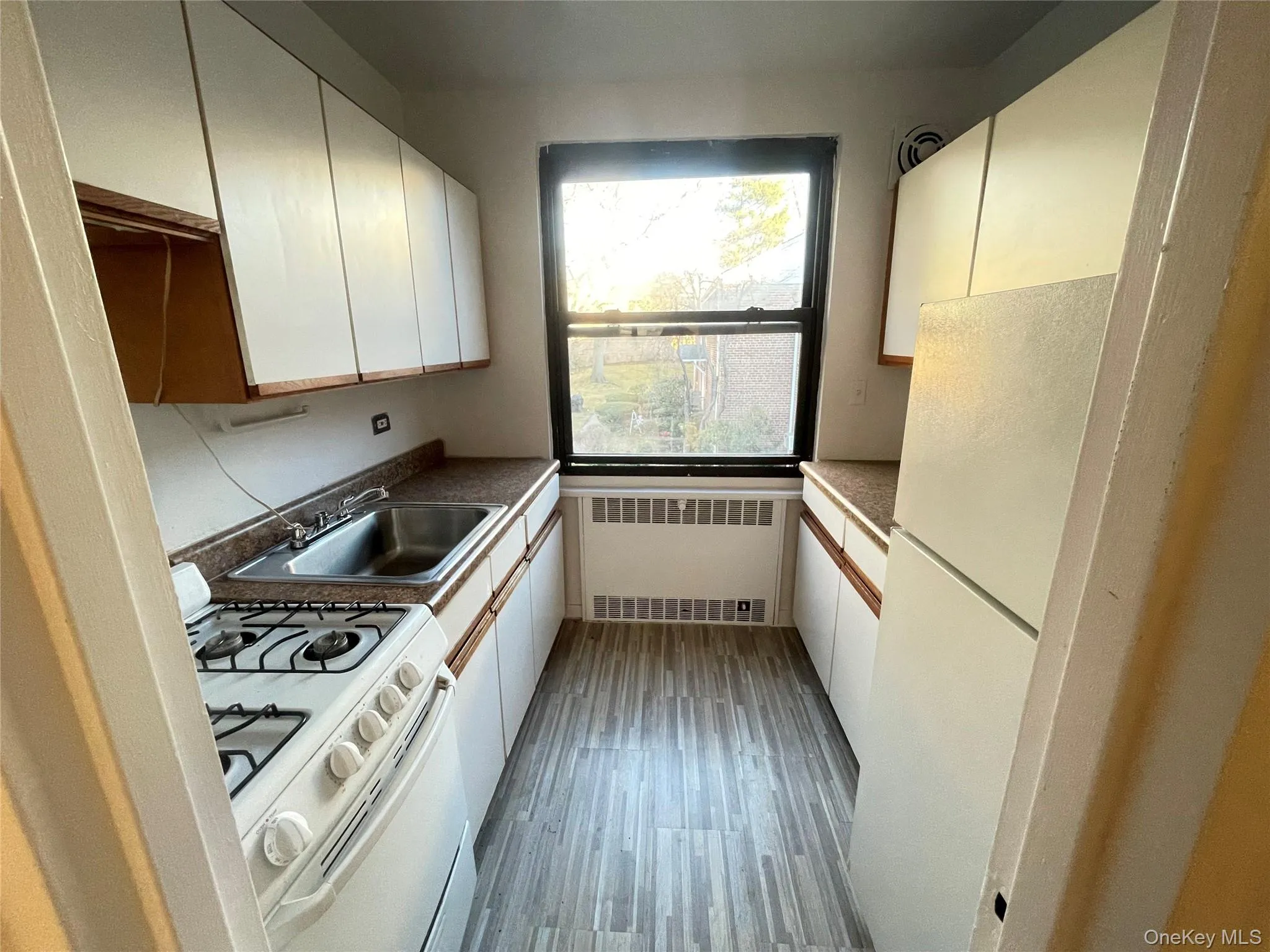 Kitchen with white appliances, radiator heating unit, white cabinets, dark wood-type flooring, and dark countertops Kitchen with white appliances, radiator heating unit, white cabinets, dark wood-type flooring, and dark countertops