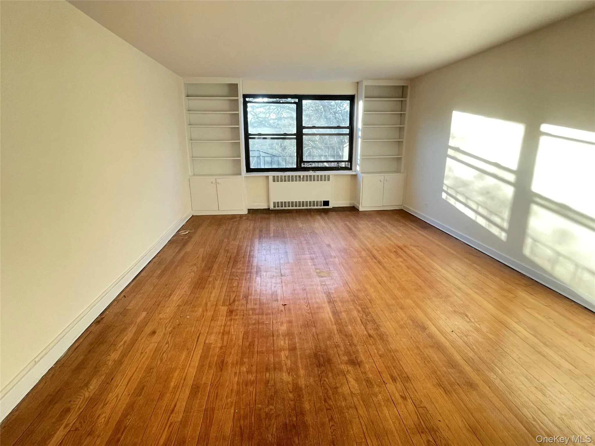 Empty room featuring built in features, radiator heating unit, and light wood-style flooring Empty room featuring built in features, radiator heating unit, and light wood-style flooring