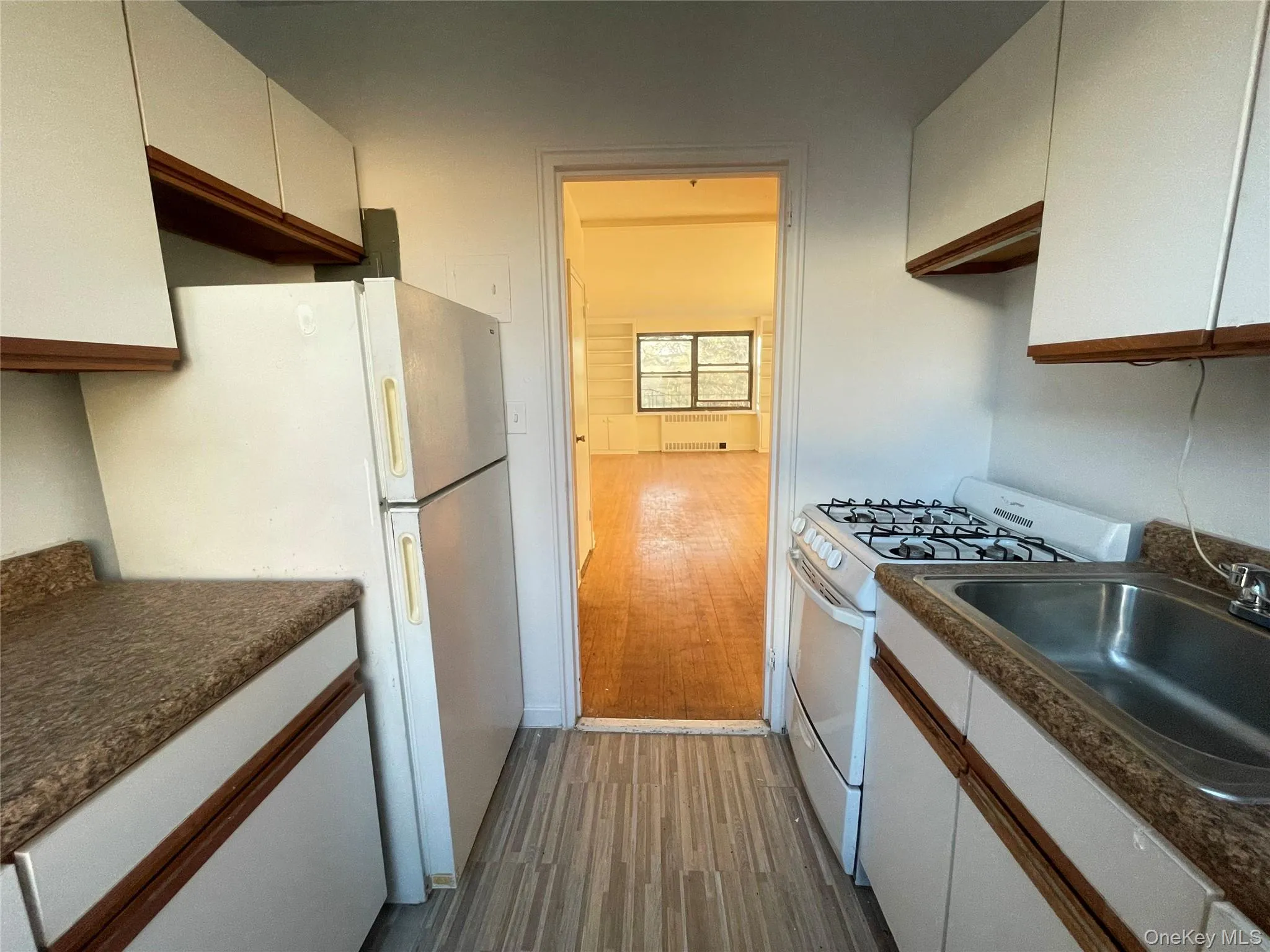 Kitchen featuring white cabinets, white appliances, dark countertops, dark wood-style floors, and radiator Kitchen featuring white cabinets, white appliances, dark countertops, dark wood-style floors, and radiator