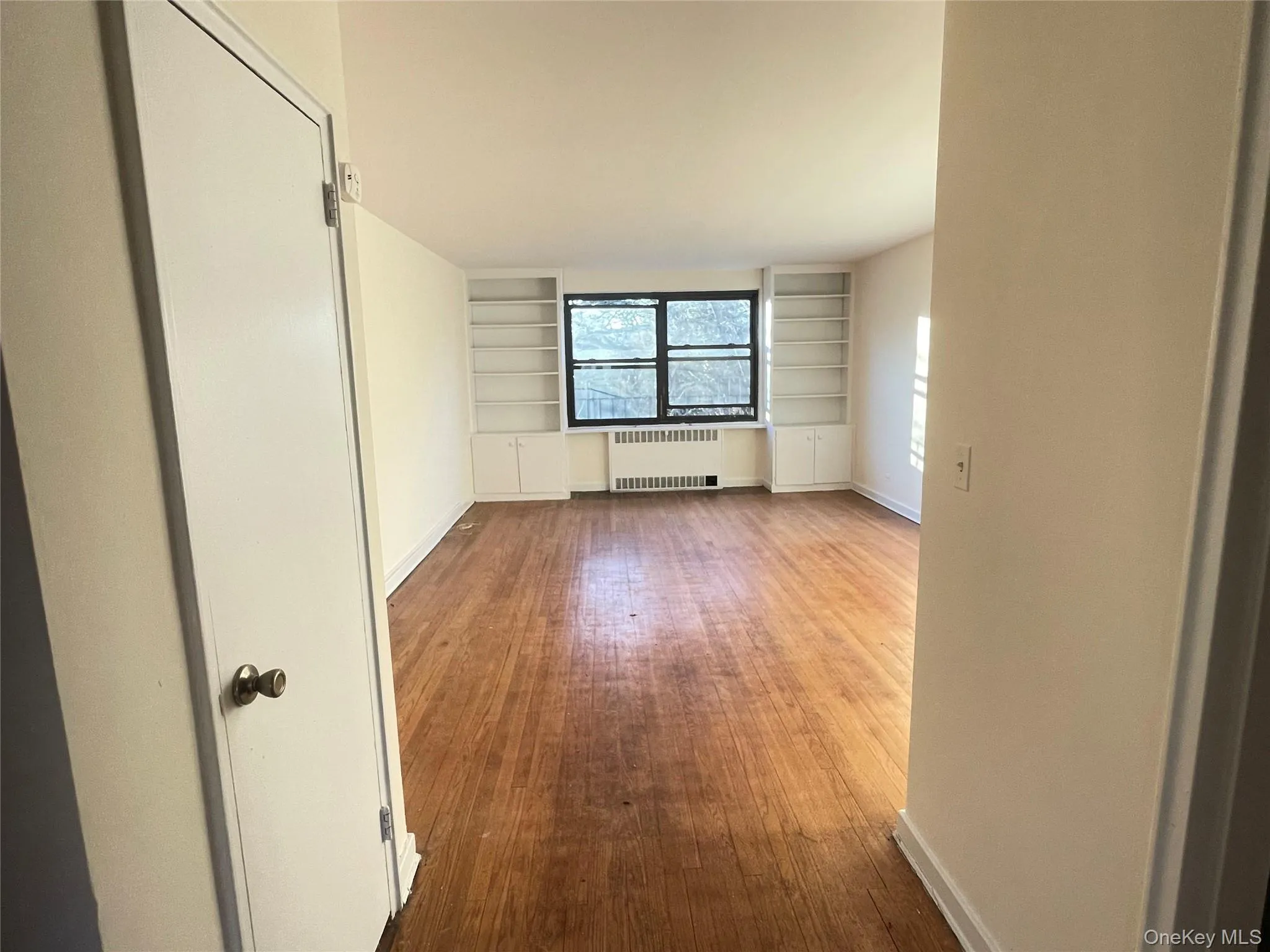 Unfurnished room featuring radiator, built in shelves, and dark wood finished floors Unfurnished room featuring radiator, built in shelves, and dark wood finished floors