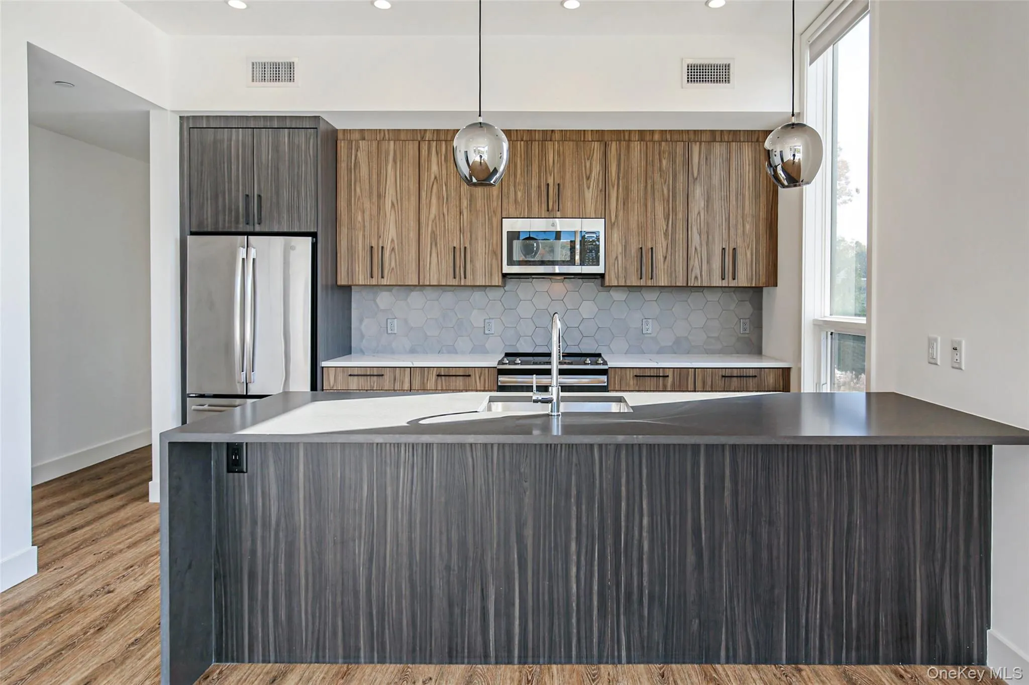 Kitchen featuring sink, light hardwood / wood-style flooring, pendant lighting, stainless steel appliances, and decorative backsplash Kitchen featuring sink, light hardwood / wood-style flooring, pendant lighting, stainless steel appliances, and decorative backsplash