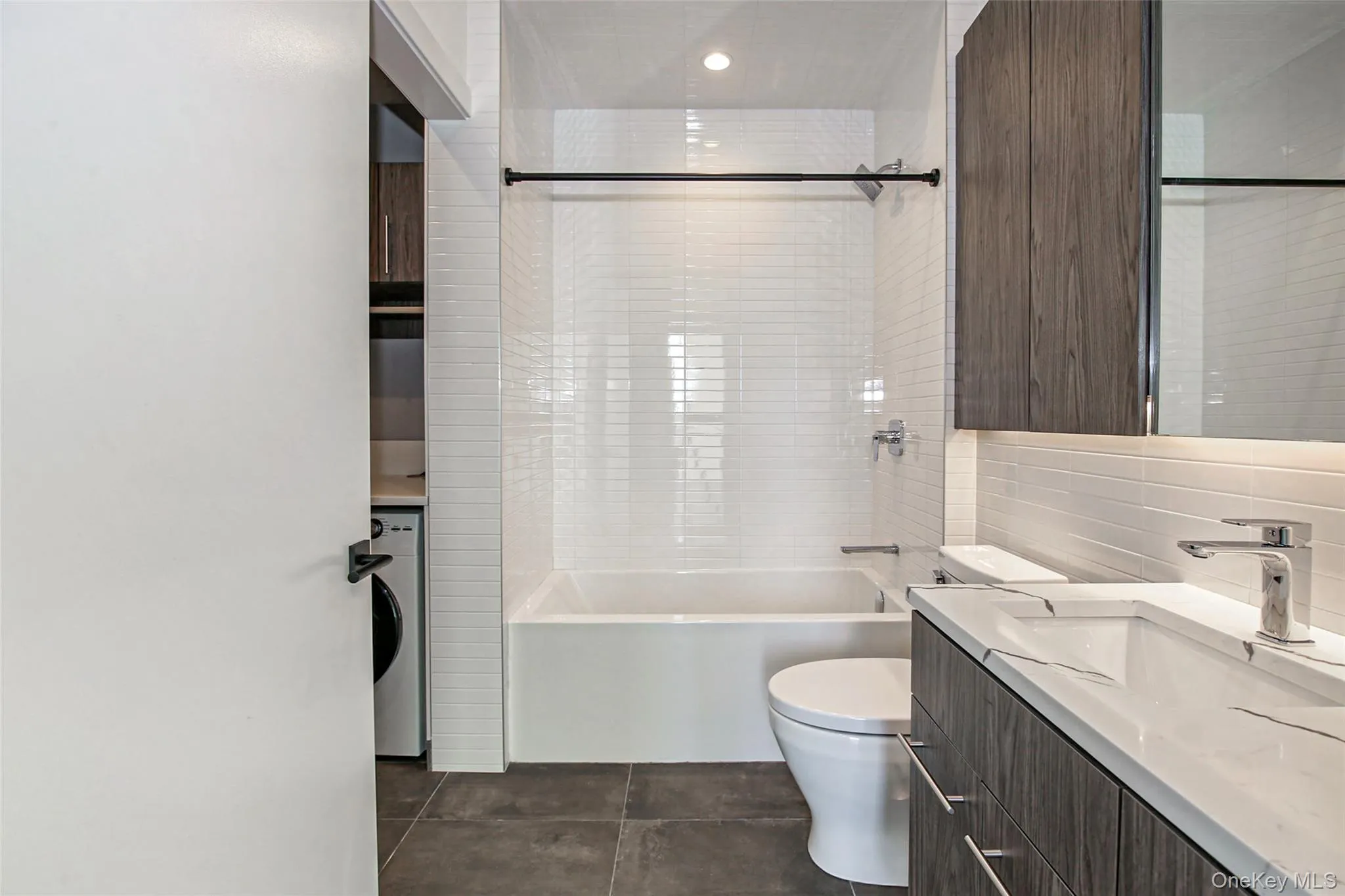 Full bathroom with tile patterned floors, toilet, tile walls, vanity, and tiled shower / bath combo Full bathroom with tile patterned floors, toilet, tile walls, vanity, and tiled shower / bath combo