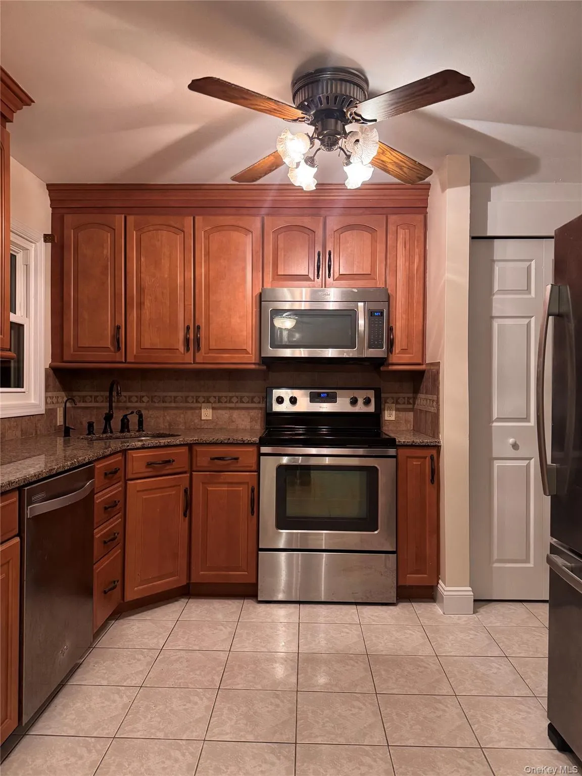 Kitchen featuring appliances with stainless steel finishes, light tile patterned flooring, backsplash, and dark stone counters Kitchen featuring appliances with stainless steel finishes, light tile patterned flooring, backsplash, and dark stone counters