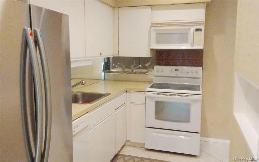 Kitchen with white appliances, light countertops, backsplash, light tile patterned flooring, and white cabinets Kitchen with white appliances, light countertops, backsplash, light tile patterned flooring, and white cabinets