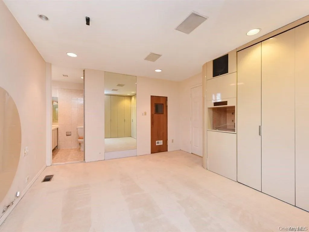 Unfurnished bedroom with recessed lighting, light colored carpet, ensuite bathroom, and multiple closets Unfurnished bedroom with recessed lighting, light colored carpet, ensuite bathroom, and multiple closets