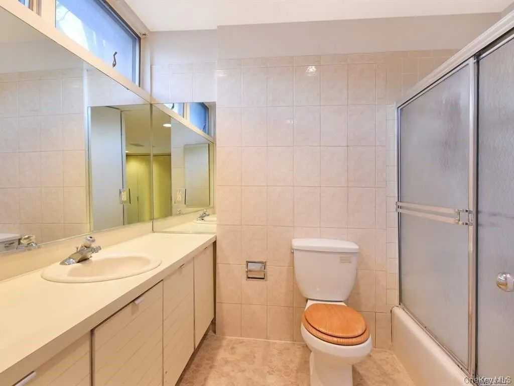 Bathroom featuring vanity, tile walls, light tile patterned floors, and combined bath / shower with glass door Bathroom featuring vanity, tile walls, light tile patterned floors, and combined bath / shower with glass door