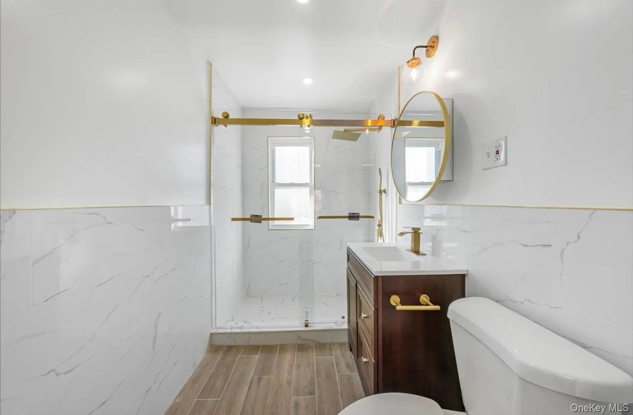 Bathroom featuring wainscoting, vanity, tile walls, a marble finish shower, and wood tiled floors Bathroom featuring wainscoting, vanity, tile walls, a marble finish shower, and wood tiled floors
