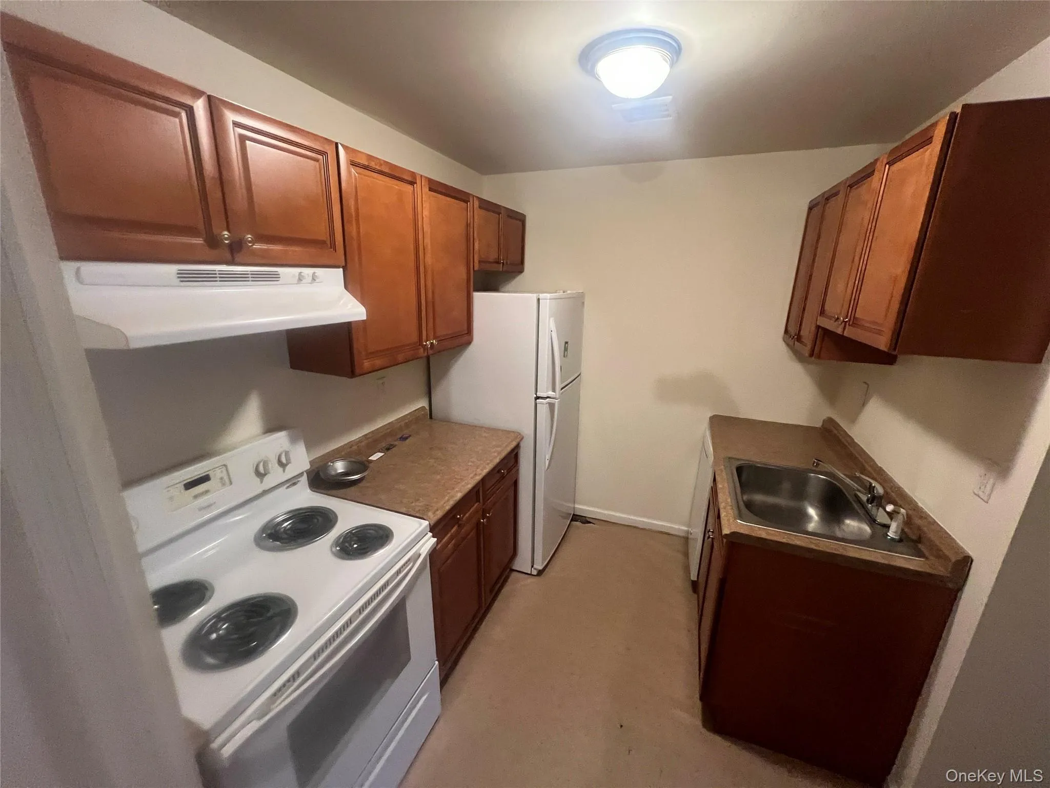 Kitchen featuring white appliances, range hood, brown cabinets, and finished concrete floors Kitchen featuring white appliances, range hood, brown cabinets, and finished concrete floors