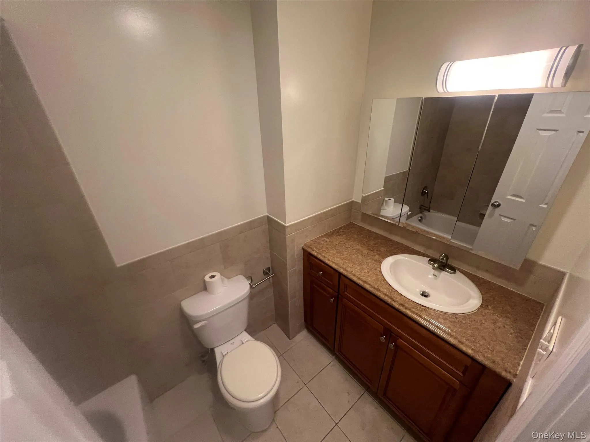 Bathroom featuring bathtub / shower combination, vanity, light tile patterned floors, a wainscoted wall, and tile walls Bathroom featuring bathtub / shower combination, vanity, light tile patterned floors, a wainscoted wall, and tile walls