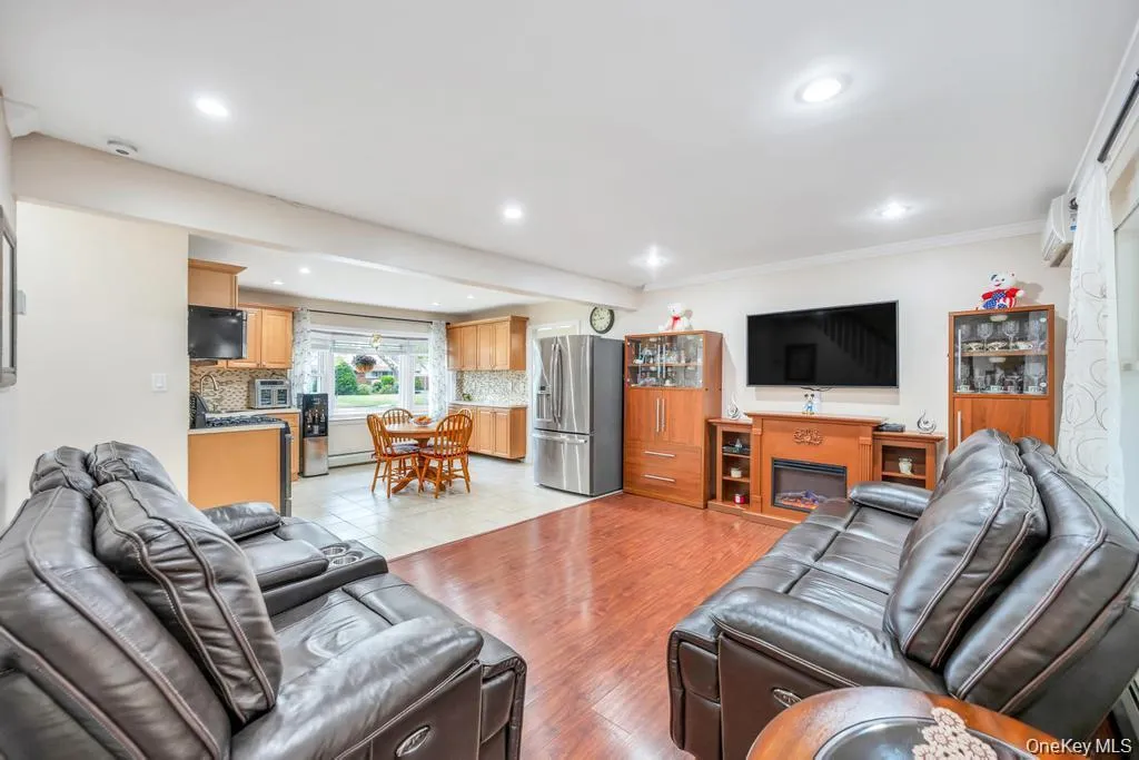 Living area featuring a glass covered fireplace, light wood-type flooring, ornamental molding, an AC wall unit, and recessed lighting Living area featuring a glass covered fireplace, light wood-type flooring, ornamental molding, an AC wall unit, and recessed lighting