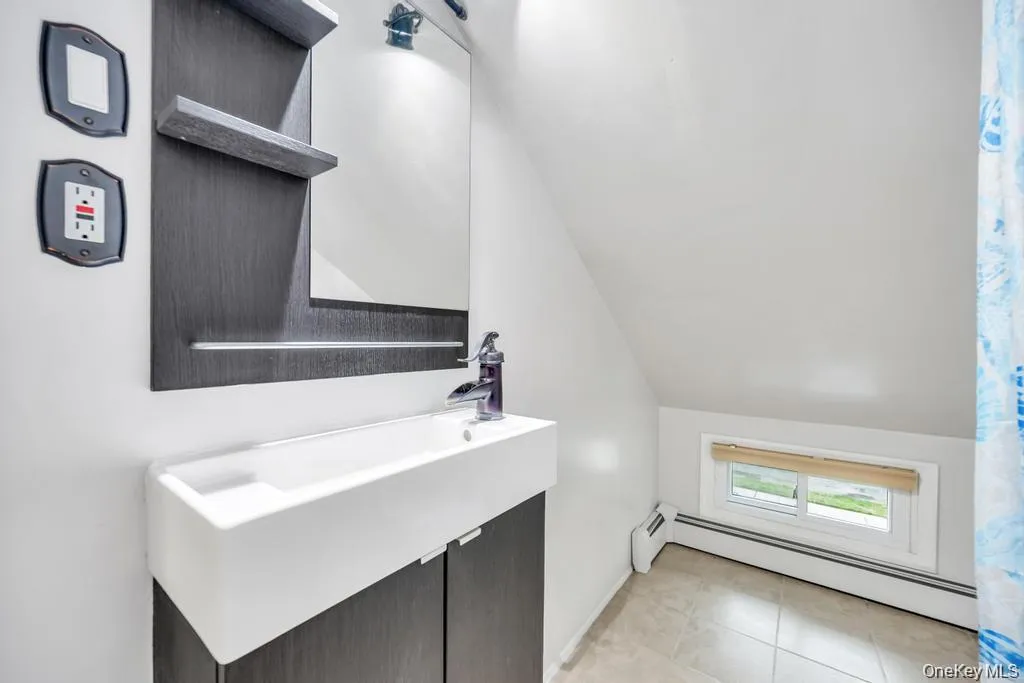 Bathroom with a baseboard radiator, vanity, vaulted ceiling, and light tile patterned floors Bathroom with a baseboard radiator, vanity, vaulted ceiling, and light tile patterned floors