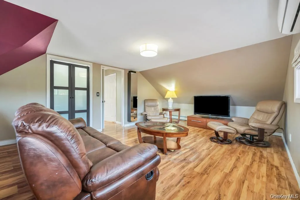 Living room featuring a wall unit AC, light wood-type flooring, french doors, and lofted ceiling Living room featuring a wall unit AC, light wood-type flooring, french doors, and lofted ceiling