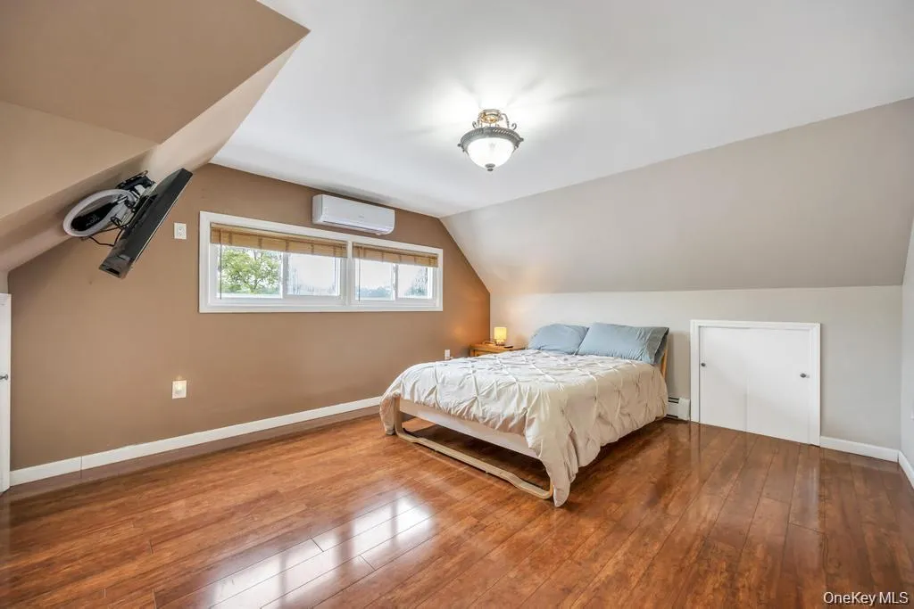Bedroom with vaulted ceiling, hardwood / wood-style flooring, a wall mounted AC, and baseboard heating Bedroom with vaulted ceiling, hardwood / wood-style flooring, a wall mounted AC, and baseboard heating
