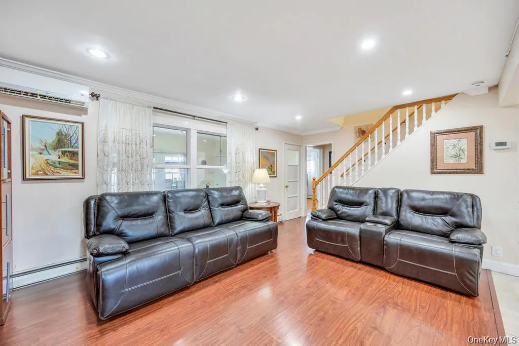 Living room featuring stairs, ornamental molding, wood finished floors, an AC wall unit, and a baseboard heating unit Living room featuring stairs, ornamental molding, wood finished floors, an AC wall unit, and a baseboard heating unit