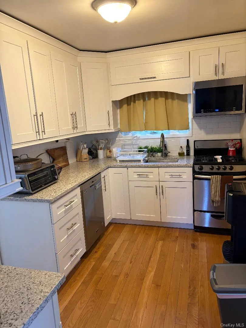Kitchen with white cabinets, stainless steel appliances, and light wood finished floors Kitchen with white cabinets, stainless steel appliances, and light wood finished floors