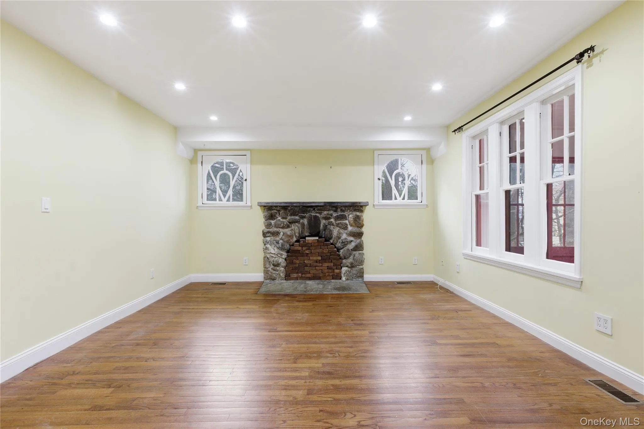 Unfurnished living room featuring wood-type flooring, recessed lighting, and a stone fireplace Unfurnished living room featuring wood-type flooring, recessed lighting, and a stone fireplace