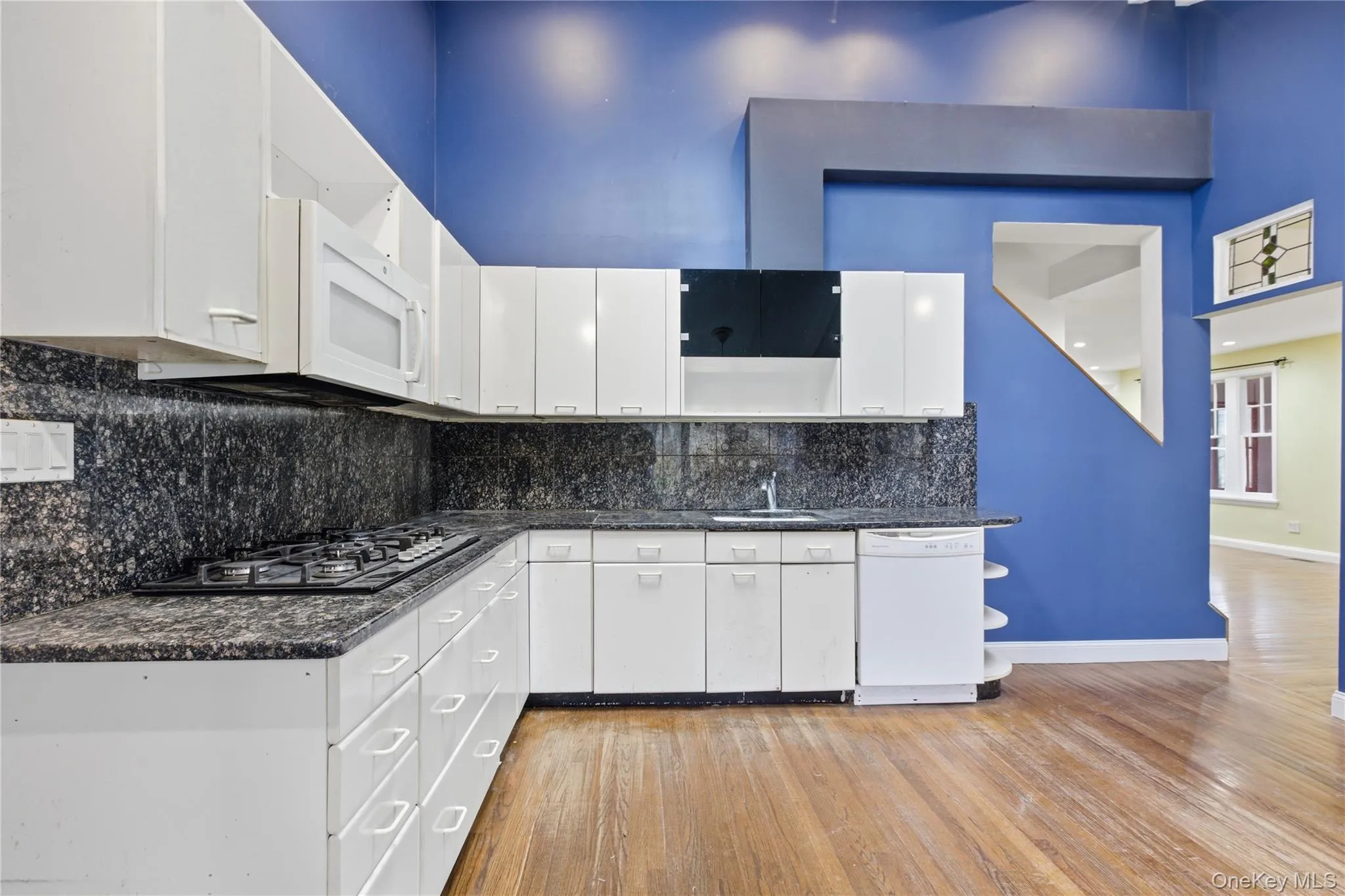 Kitchen featuring open shelves, white cabinetry, white appliances, light wood finished floors, and dark stone countertops Kitchen featuring open shelves, white cabinetry, white appliances, light wood finished floors, and dark stone countertops