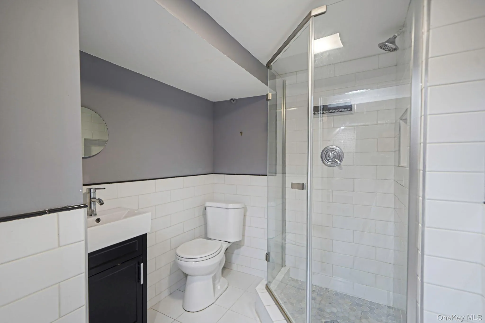 Bathroom featuring tile walls, vanity, a shower stall, tile patterned floors, and a wainscoted wall Bathroom featuring tile walls, vanity, a shower stall, tile patterned floors, and a wainscoted wall