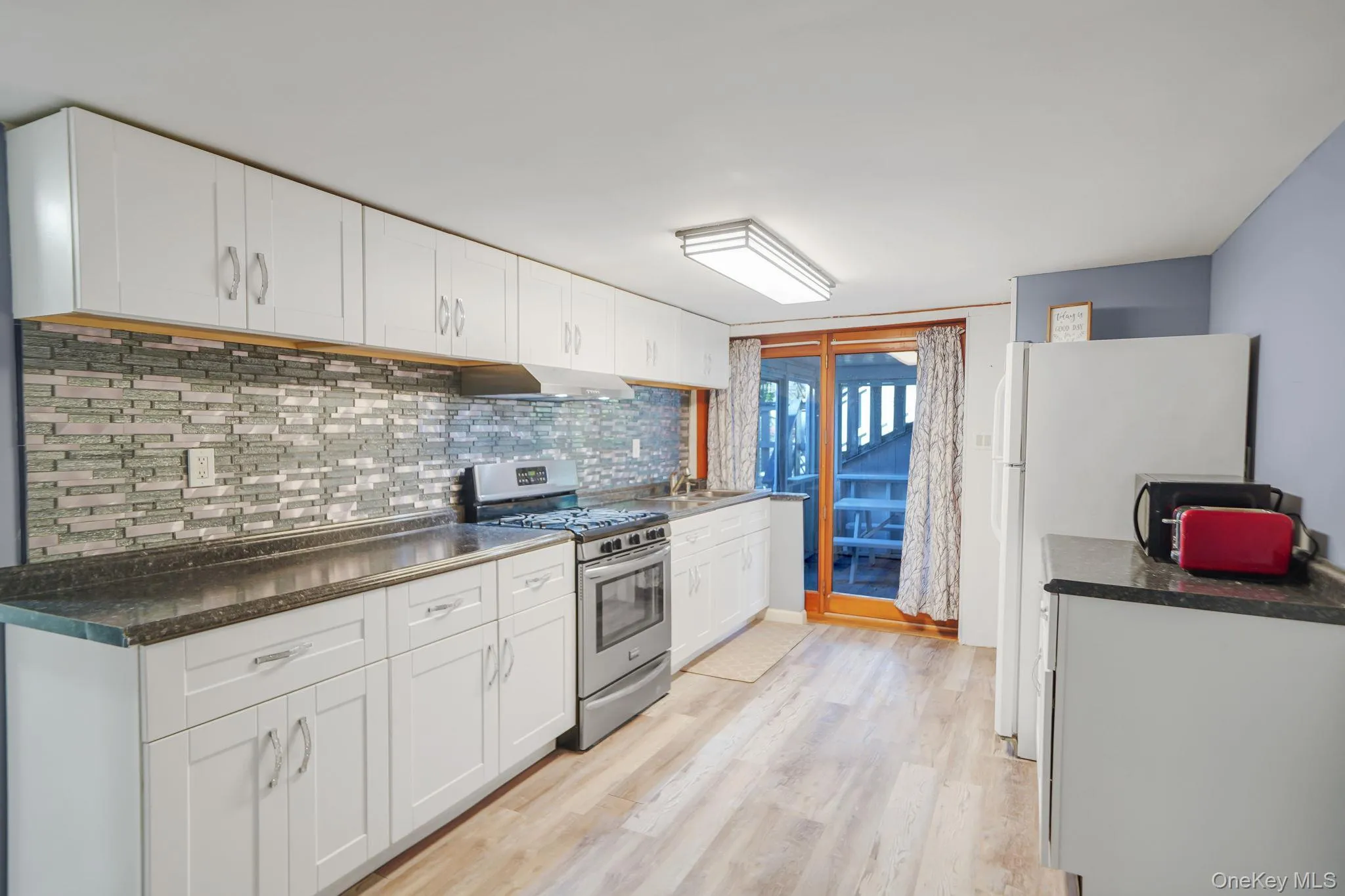 Kitchen with stainless steel gas range oven, white cabinets, freestanding refrigerator, and decorative backsplash Kitchen with stainless steel gas range oven, white cabinets, freestanding refrigerator, and decorative backsplash