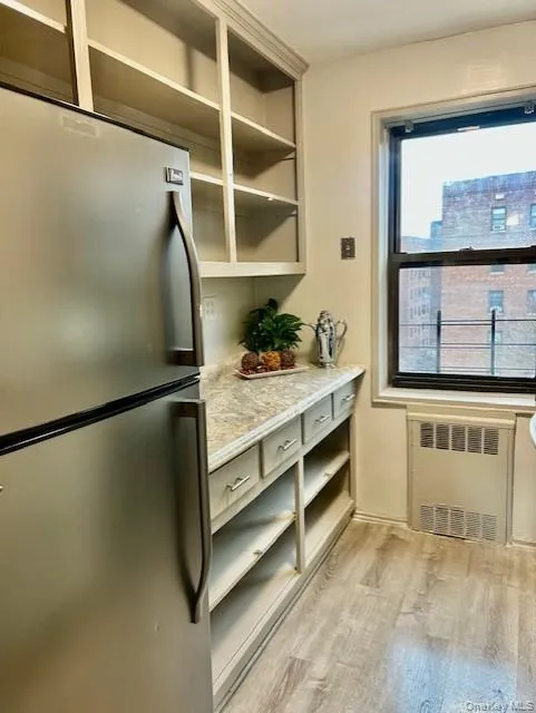 Kitchen with freestanding refrigerator, open shelves, light wood-type flooring, radiator heating unit, and light stone counters Kitchen with freestanding refrigerator, open shelves, light wood-type flooring, radiator heating unit, and light stone counters