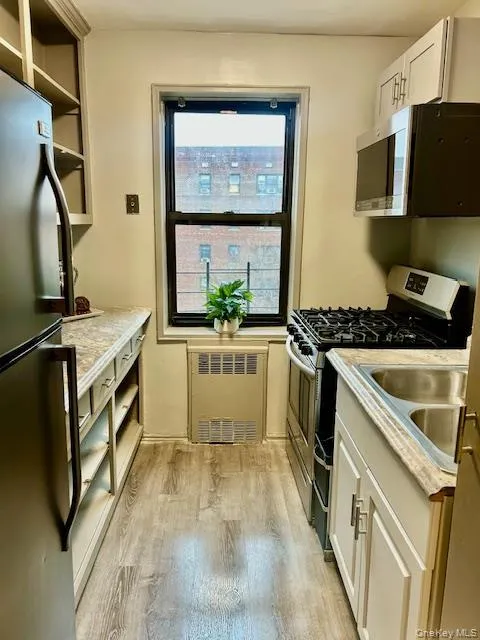 Kitchen featuring appliances with stainless steel finishes, white cabinetry, light countertops, light wood finished floors, and radiator heating unit Kitchen featuring appliances with stainless steel finishes, white cabinetry, light countertops, light wood finished floors, and radiator heating unit
