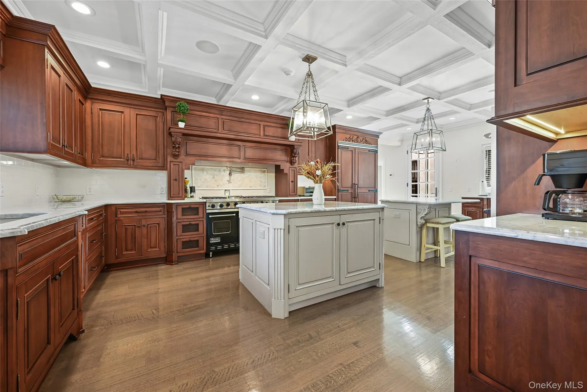 Kitchen featuring backsplash, hanging light fixtures, light stone countertops, coffered ceiling, and white cabinetry Kitchen featuring backsplash, hanging light fixtures, light stone countertops, coffered ceiling, and white cabinetry