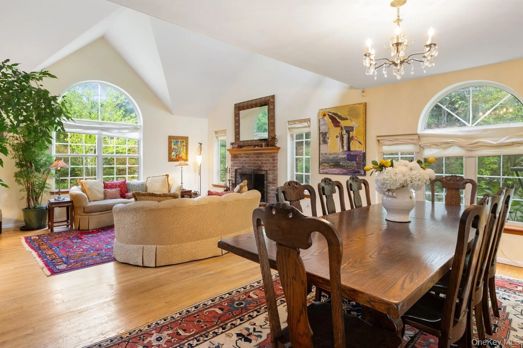 Dining room with a brick fireplace, light wood-type flooring, a chandelier, and high vaulted ceiling Dining room with a brick fireplace, light wood-type flooring, a chandelier, and high vaulted ceiling