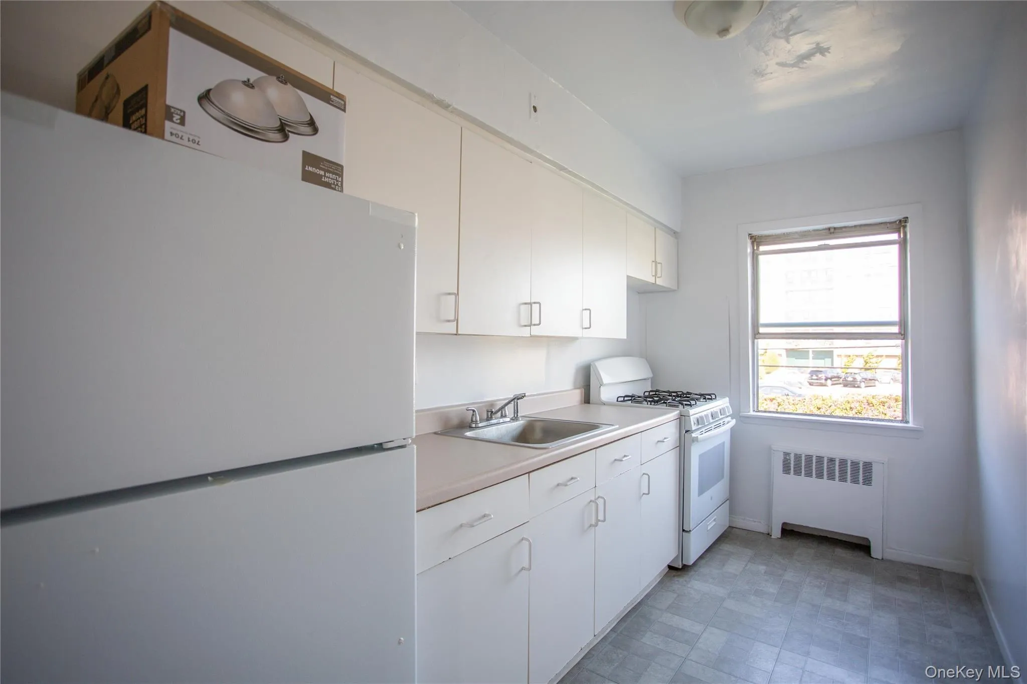 Kitchen with white appliances, radiator heating unit, light countertops, and white cabinets Kitchen with white appliances, radiator heating unit, light countertops, and white cabinets