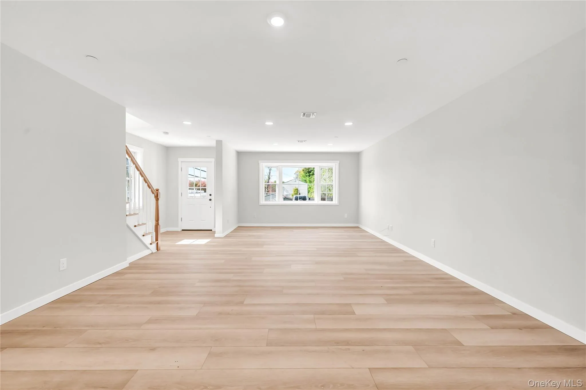 Unfurnished living room with stairway, light wood-type flooring, and recessed lighting Unfurnished living room with stairway, light wood-type flooring, and recessed lighting