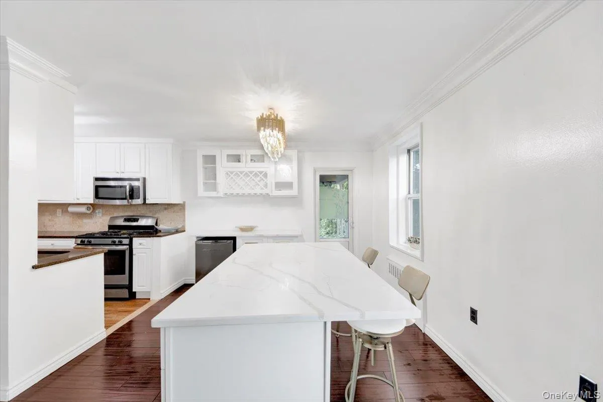 Kitchen with a kitchen bar, backsplash, stainless steel appliances, dark stone counters, and white cabinets Kitchen with a kitchen bar, backsplash, stainless steel appliances, dark stone counters, and white cabinets