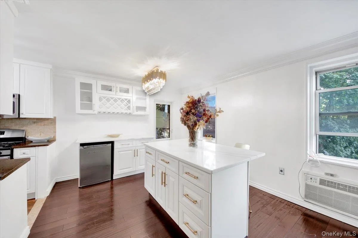 Kitchen with white cabinetry, stainless steel appliances, dark wood-style floors, dark stone countertops, and ornamental molding Kitchen with white cabinetry, stainless steel appliances, dark wood-style floors, dark stone countertops, and ornamental molding