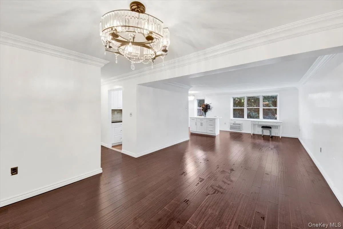 Unfurnished living room featuring ornamental molding, dark wood finished floors, radiator heating unit, and a chandelier Unfurnished living room featuring ornamental molding, dark wood finished floors, radiator heating unit, and a chandelier