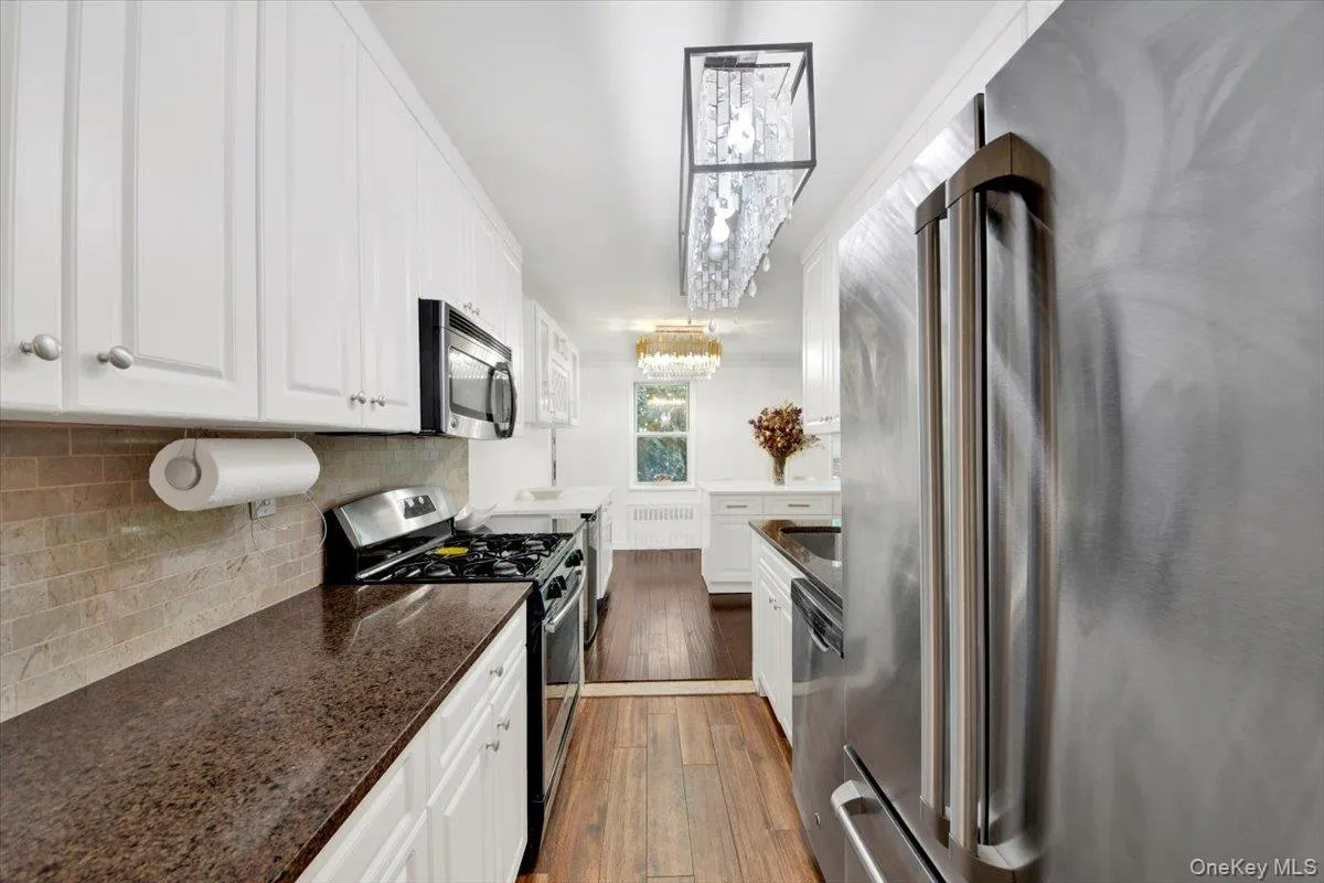 Kitchen with appliances with stainless steel finishes, white cabinets, dark wood-style flooring, and tasteful backsplash Kitchen with appliances with stainless steel finishes, white cabinets, dark wood-style flooring, and tasteful backsplash