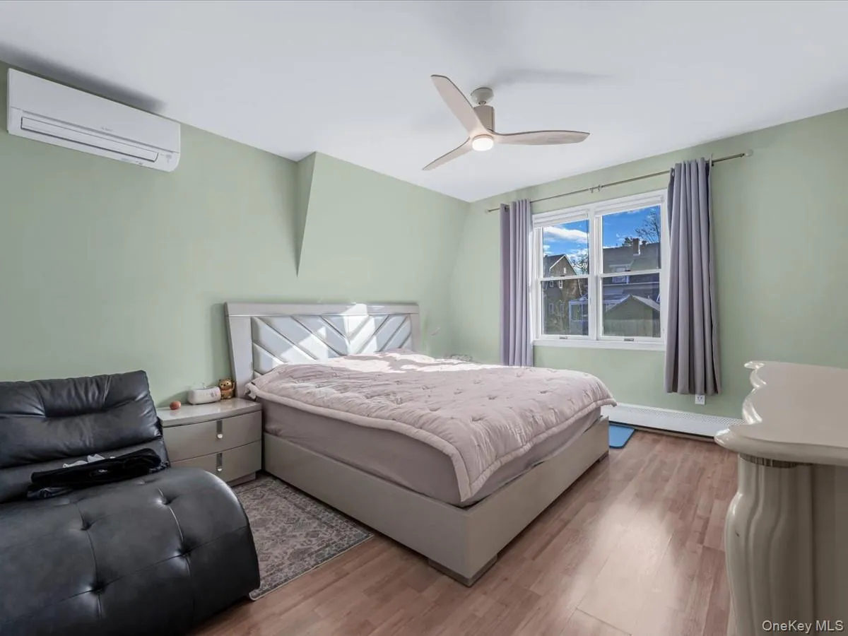 Bedroom with a wall unit AC, wood finished floors, ceiling fan, and a baseboard heating unit Bedroom with a wall unit AC, wood finished floors, ceiling fan, and a baseboard heating unit