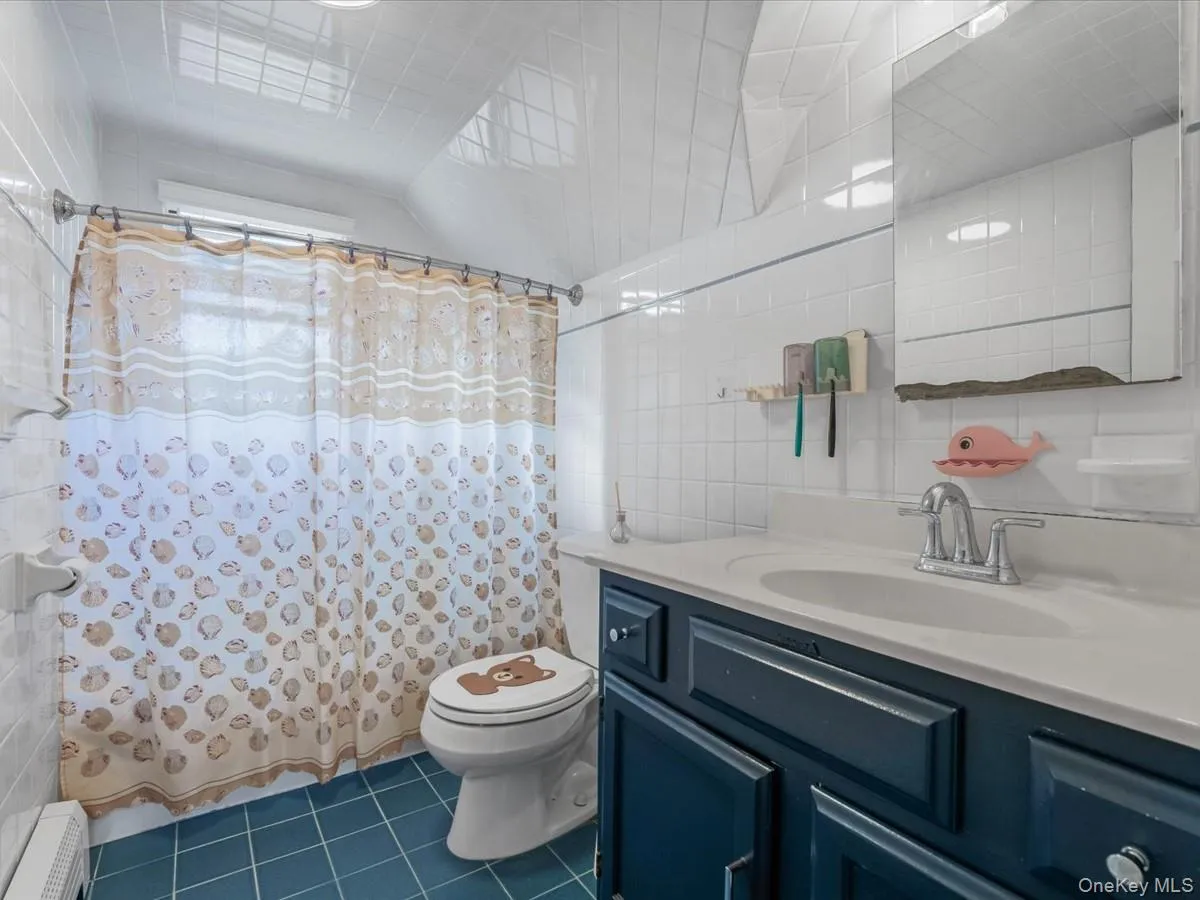 Bathroom featuring tile walls, curtained shower, vanity, dark tile patterned flooring, and a baseboard heating unit Bathroom featuring tile walls, curtained shower, vanity, dark tile patterned flooring, and a baseboard heating unit