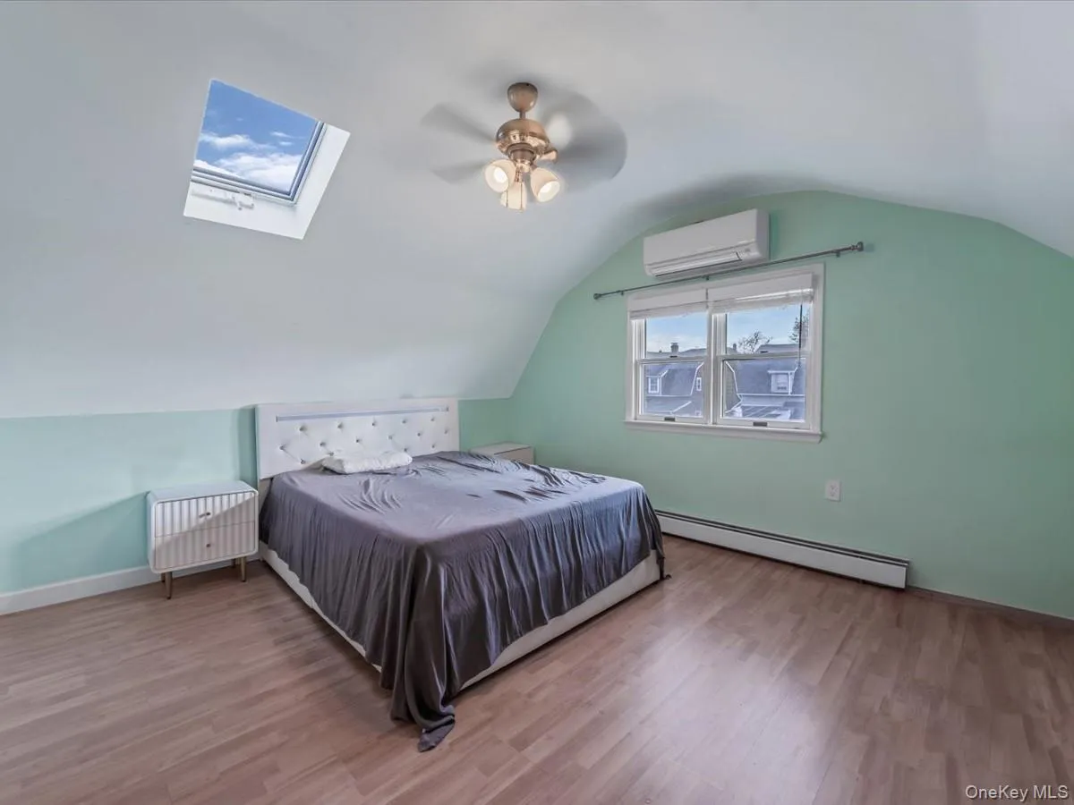 Bedroom featuring a skylight, lofted ceiling, a baseboard radiator, wood finished floors, and a wall mounted air conditioner Bedroom featuring a skylight, lofted ceiling, a baseboard radiator, wood finished floors, and a wall mounted air conditioner