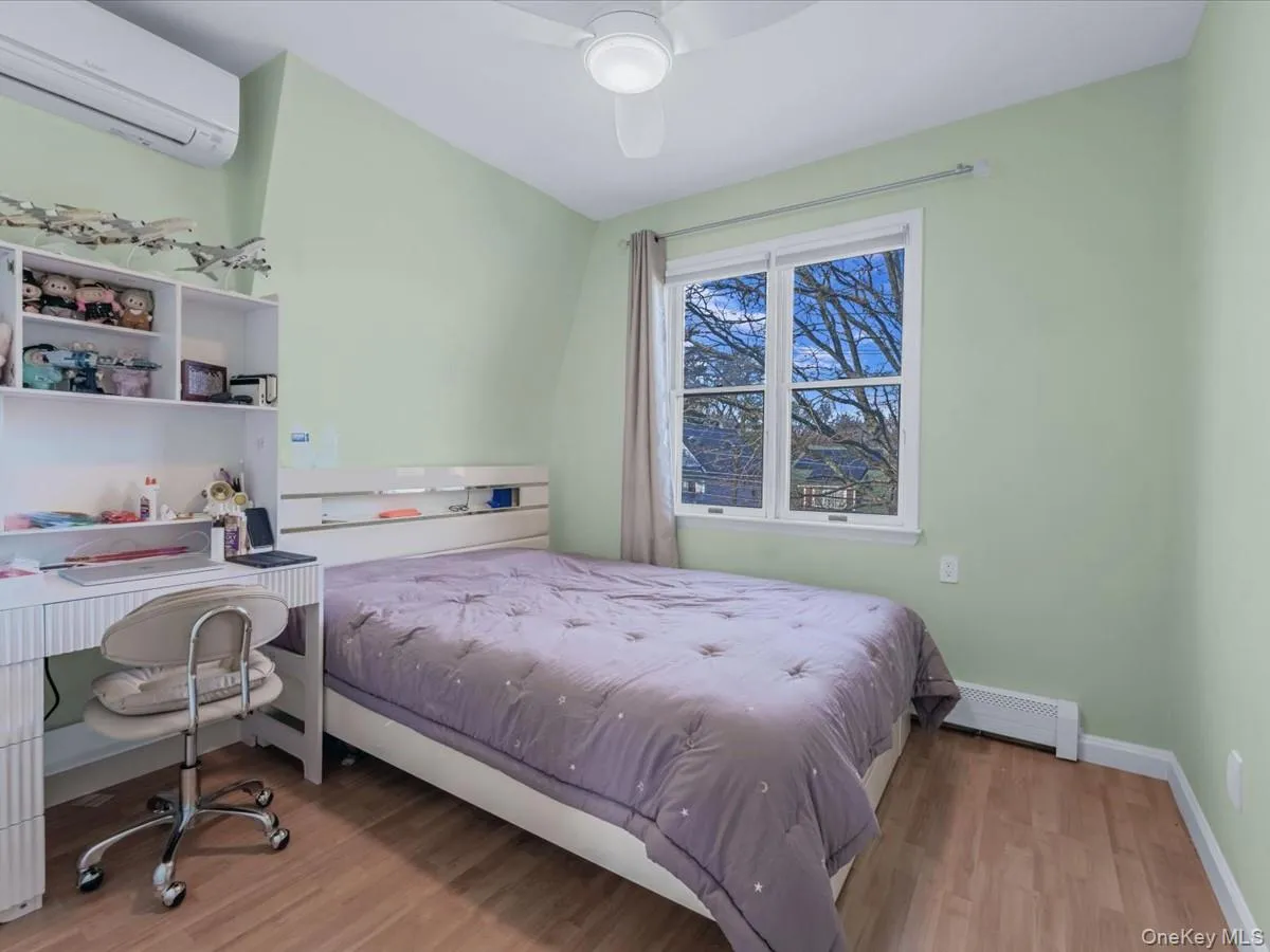 Bedroom with a wall mounted air conditioner, light wood-style floors, a baseboard radiator, ceiling fan, and an office area Bedroom with a wall mounted air conditioner, light wood-style floors, a baseboard radiator, ceiling fan, and an office area