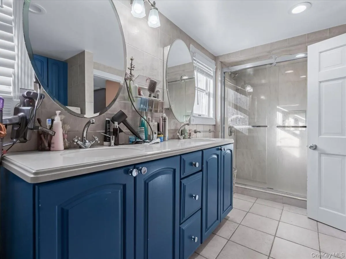 Bathroom with double vanity, light tile patterned floors, a shower stall, tile walls, and backsplash Bathroom with double vanity, light tile patterned floors, a shower stall, tile walls, and backsplash