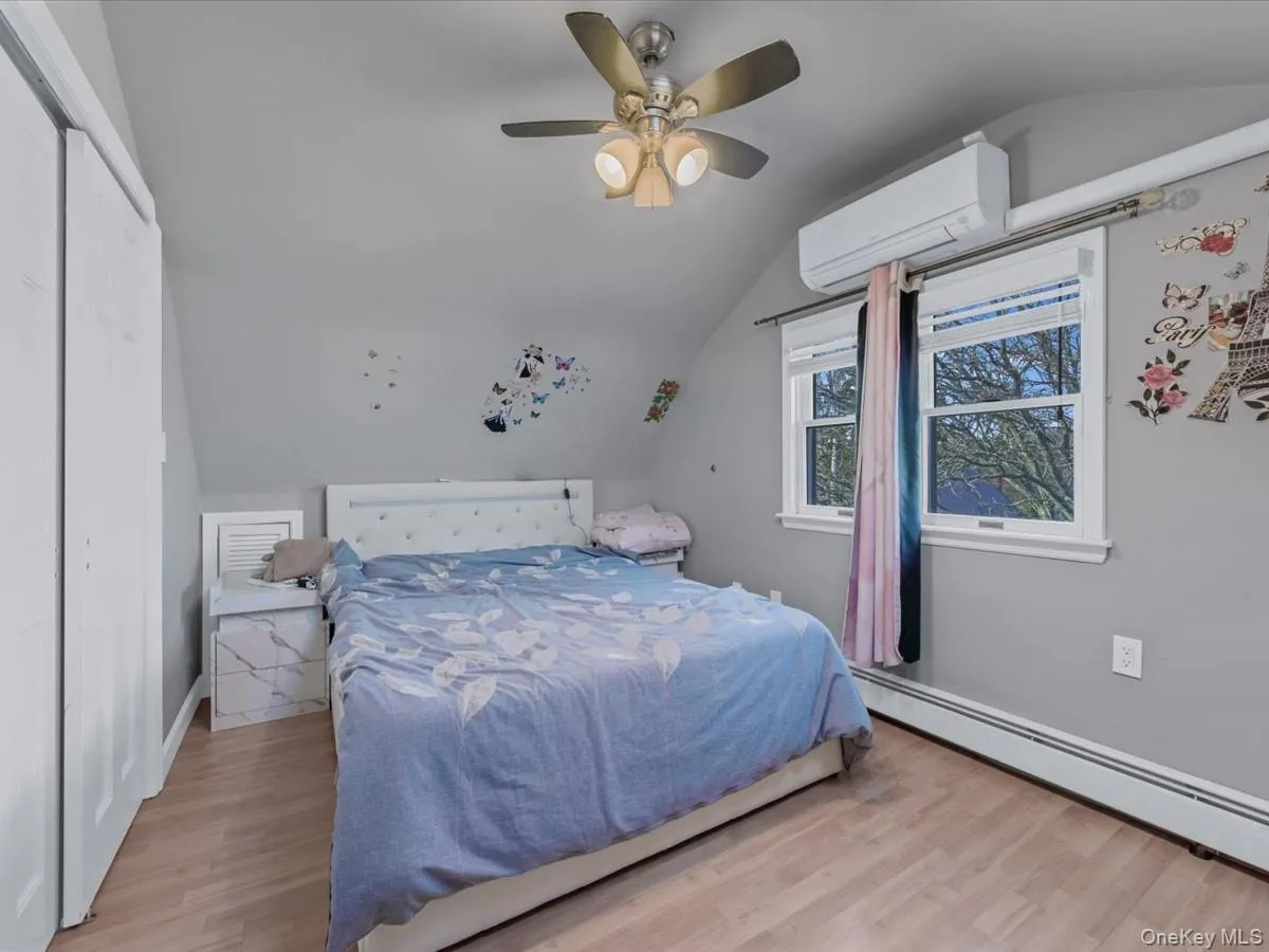 Bedroom with vaulted ceiling, a wall mounted air conditioner, light wood-style flooring, a baseboard heating unit, and a ceiling fan Bedroom with vaulted ceiling, a wall mounted air conditioner, light wood-style flooring, a baseboard heating unit, and a ceiling fan