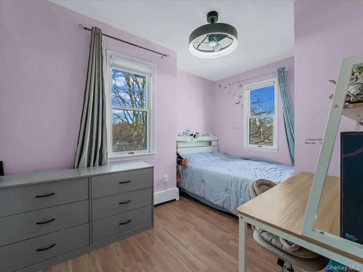 Bedroom with multiple windows, light wood-style floors, and a baseboard radiator Bedroom with multiple windows, light wood-style floors, and a baseboard radiator