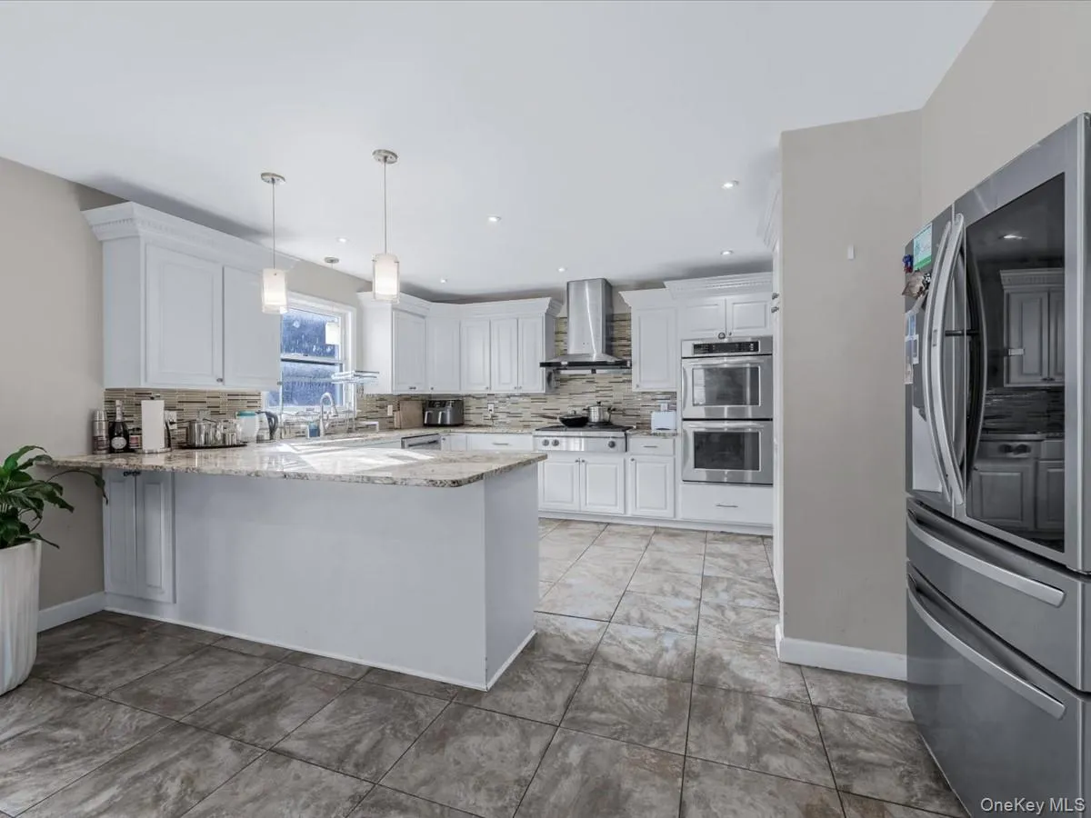 Kitchen with appliances with stainless steel finishes, light stone countertops, pendant lighting, white cabinetry, and a peninsula Kitchen with appliances with stainless steel finishes, light stone countertops, pendant lighting, white cabinetry, and a peninsula