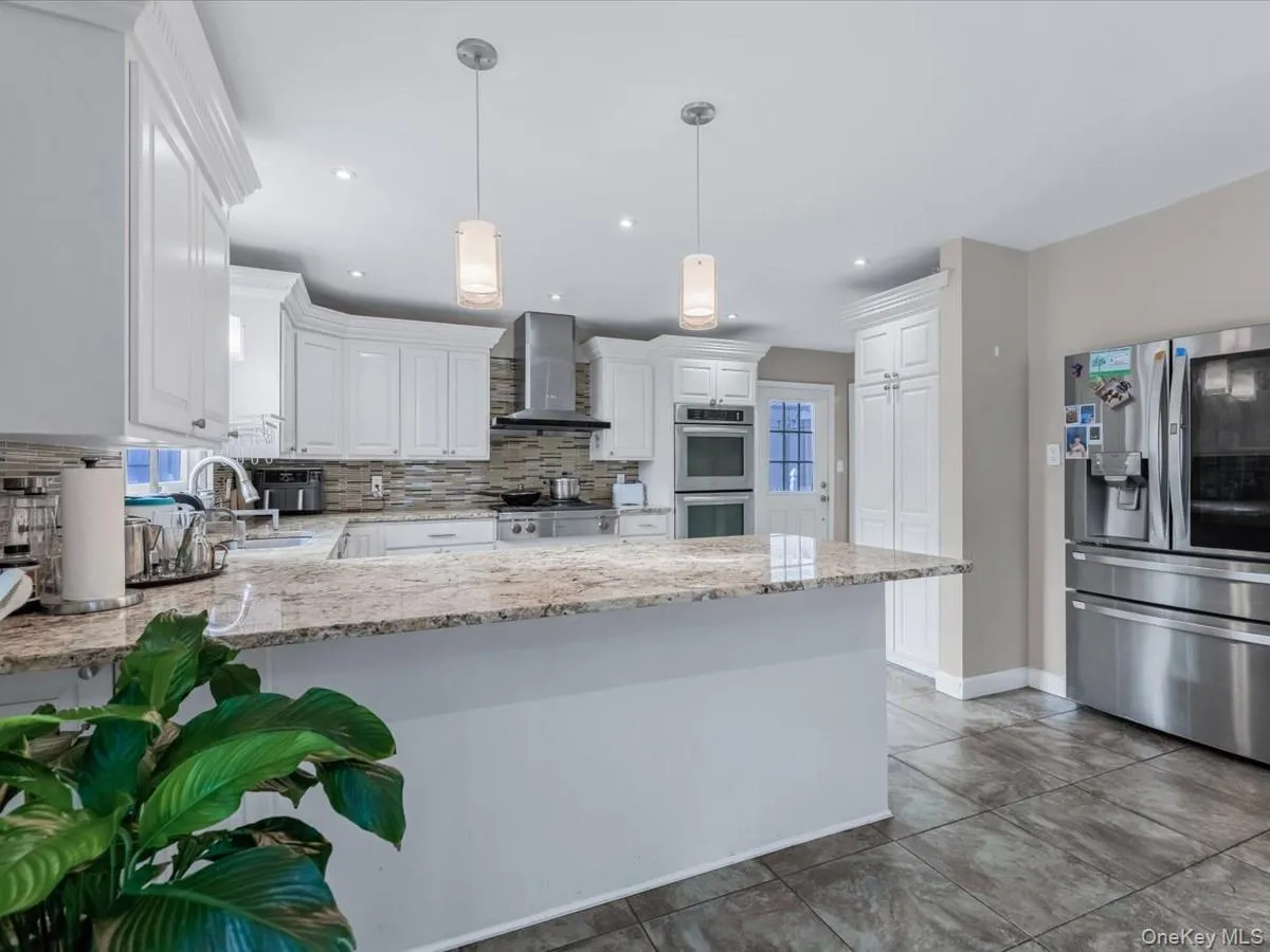 Kitchen with stainless steel appliances, white cabinets, a peninsula, light stone countertops, and wall chimney range hood Kitchen with stainless steel appliances, white cabinets, a peninsula, light stone countertops, and wall chimney range hood