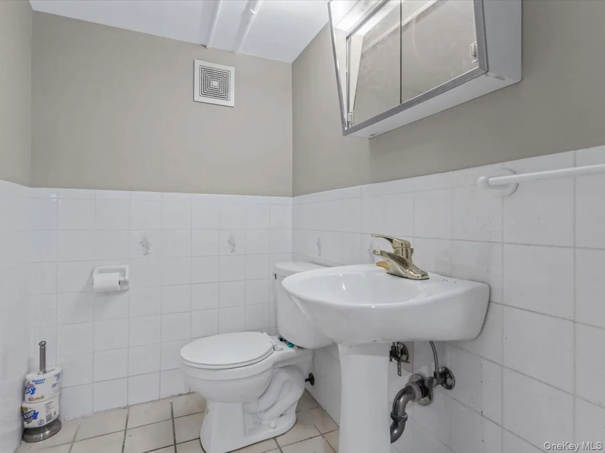 Bathroom featuring tile walls, a wainscoted wall, and light tile patterned floors Bathroom featuring tile walls, a wainscoted wall, and light tile patterned floors