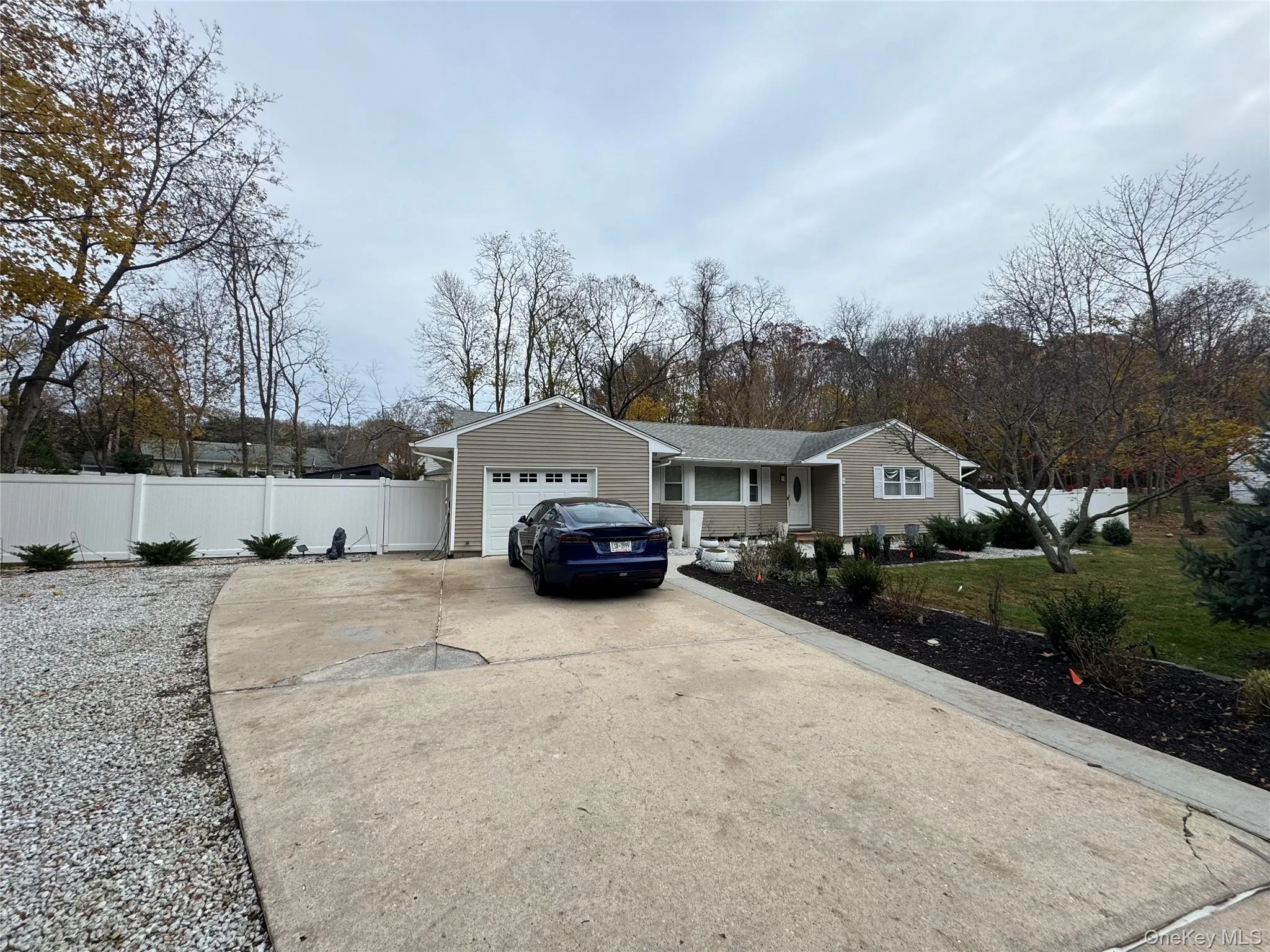 Ranch-style house featuring concrete driveway, a garage, and view of wooded area Ranch-style house featuring concrete driveway, a garage, and view of wooded area