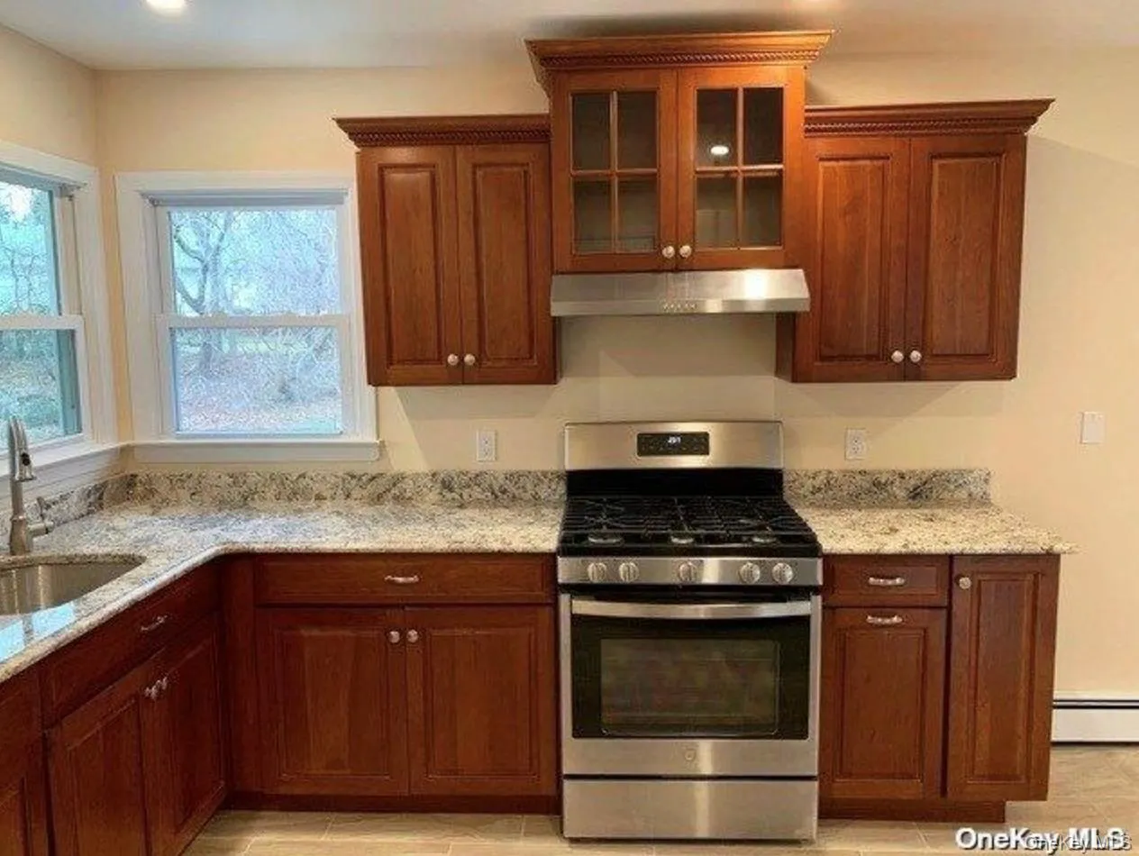 Kitchen featuring stainless steel range with gas stovetop, glass insert cabinets, and light stone counters Kitchen featuring stainless steel range with gas stovetop, glass insert cabinets, and light stone counters