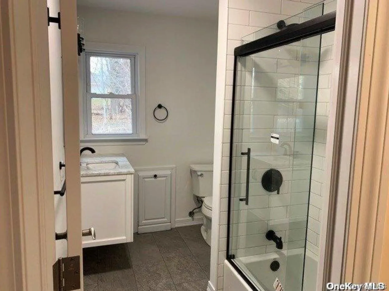 Full bathroom featuring vanity, shower / bath combination with glass door, and dark tile patterned flooring Full bathroom featuring vanity, shower / bath combination with glass door, and dark tile patterned flooring