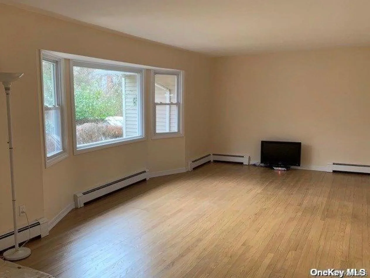 Unfurnished living room featuring light wood finished floors, baseboard heating, and healthy amount of natural light Unfurnished living room featuring light wood finished floors, baseboard heating, and healthy amount of natural light