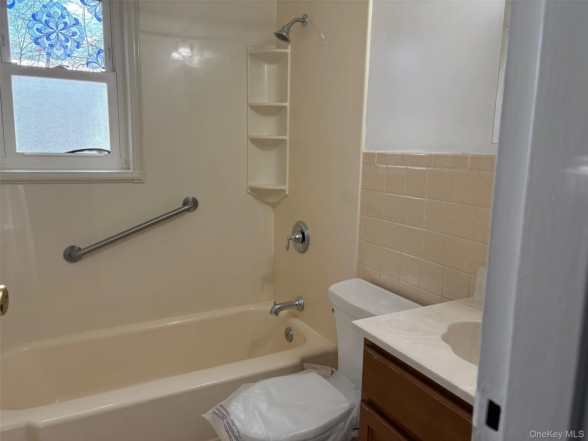 Full bathroom with tile walls, vanity, a wainscoted wall, and shower combination Full bathroom with tile walls, vanity, a wainscoted wall, and shower combination