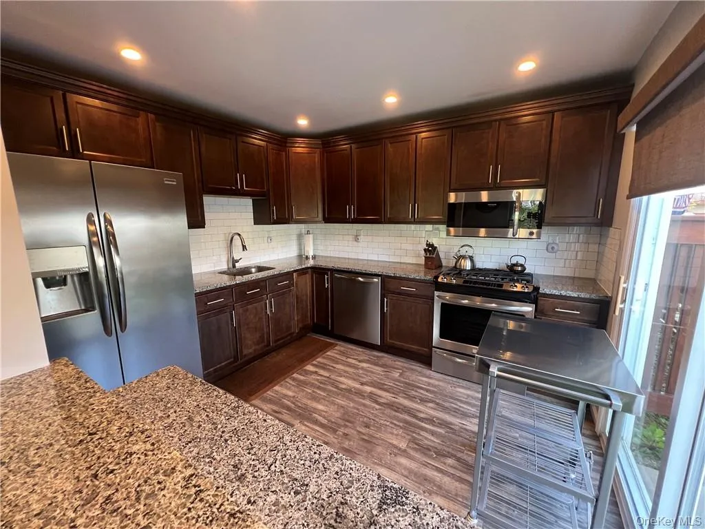 Kitchen featuring light stone counters, dark hardwood / wood-style floors, sink, stainless steel appliances, and backsplash Kitchen featuring light stone counters, dark hardwood / wood-style floors, sink, stainless steel appliances, and backsplash