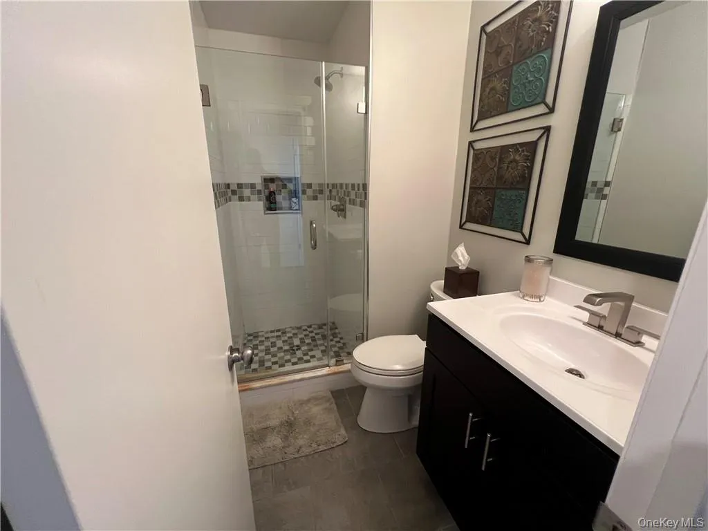 Bathroom with tile patterned flooring, a shower with shower door, vanity, and toilet Bathroom with tile patterned flooring, a shower with shower door, vanity, and toilet